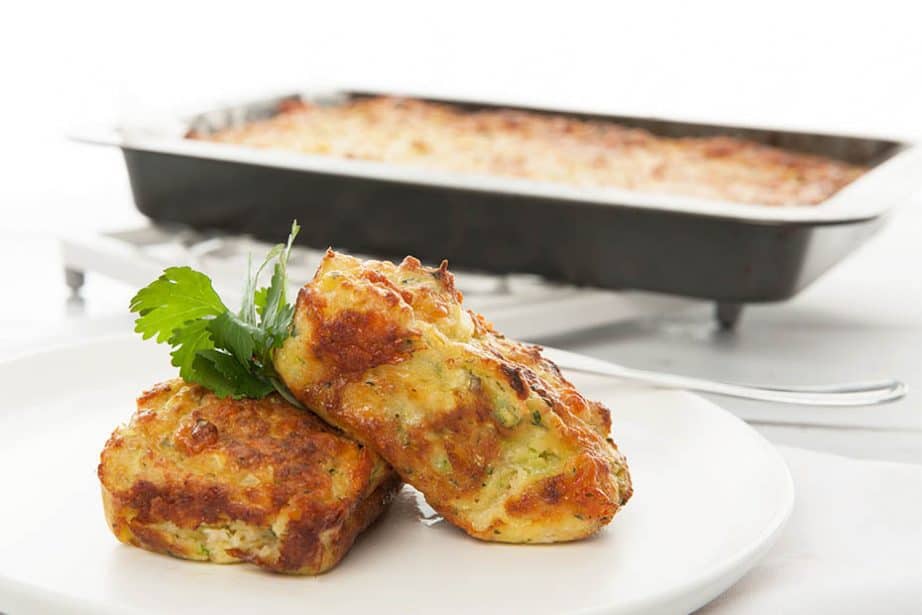 Landscape image of zucchini slice in the foreground and a large tray of slice in the background 