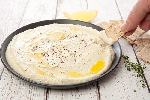 Dipping crackers into Babaganoush on a plate. Wooden background.