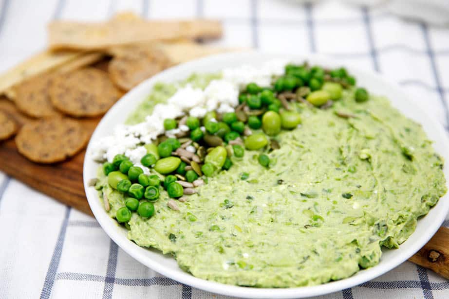 Landscape view, avocado dip on white plate with feta and pea garnish