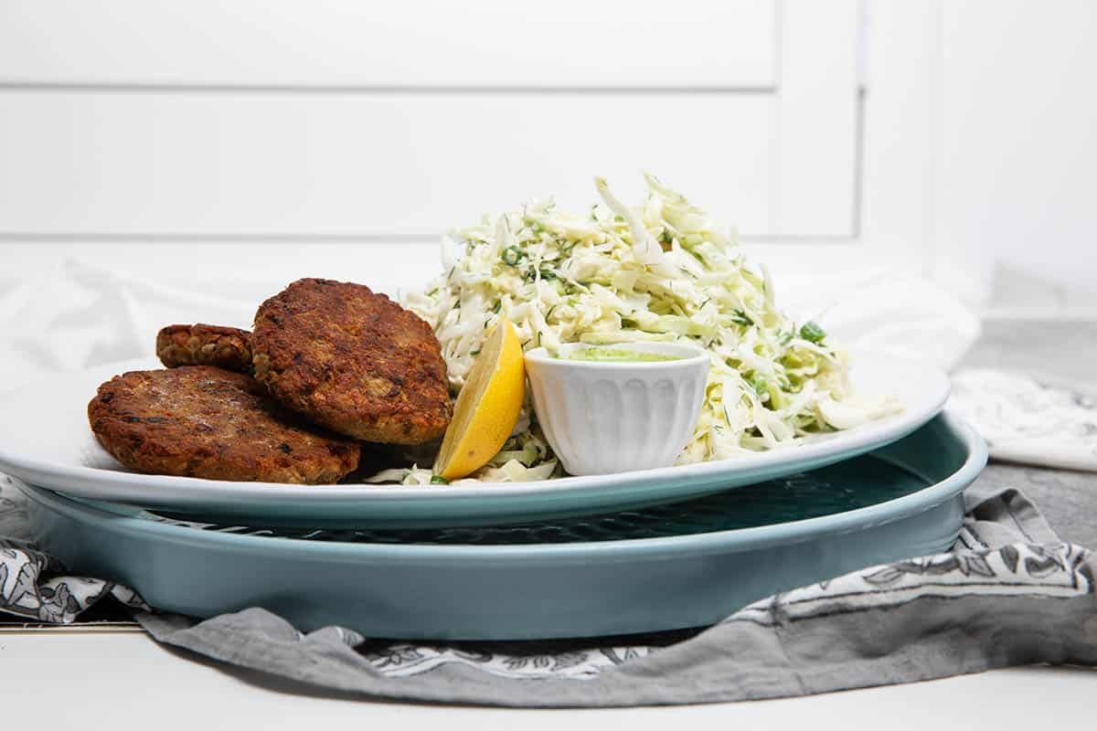 Two plates with a large serving of herbed coleslaw and salmon burger patty.
