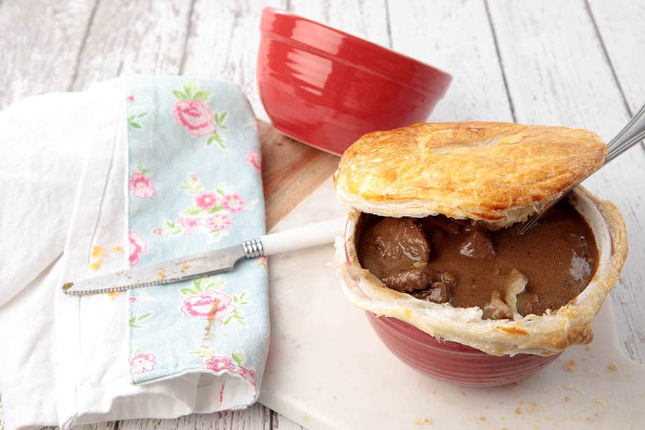 Guinness Pot Pie on a wooden background with the pastry lid partial off to reveal the filling