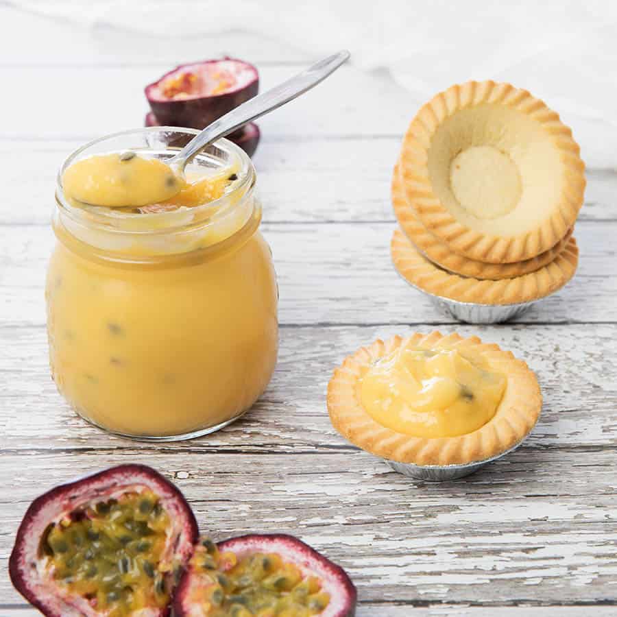 Passionfruit curd being spooned out of a jar into tartlets