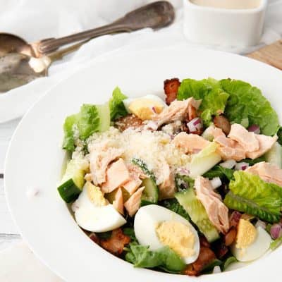 Individual serve Salmon Caesar Salad in a white bowl with dressing on the side