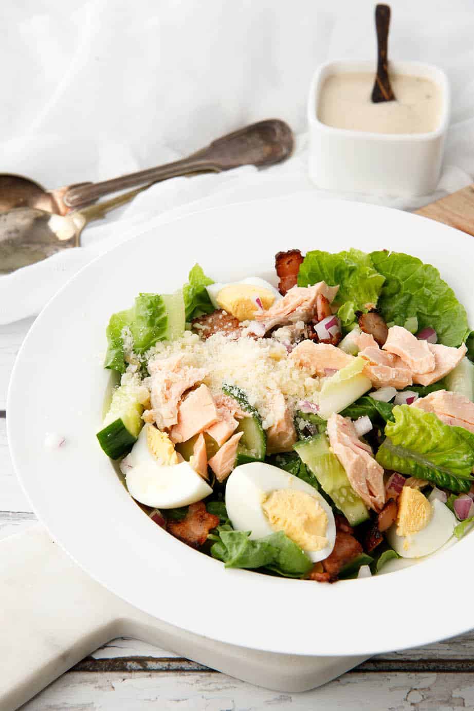 Individual serve Salmon Caesar Salad in a white bowl with dressing on the side