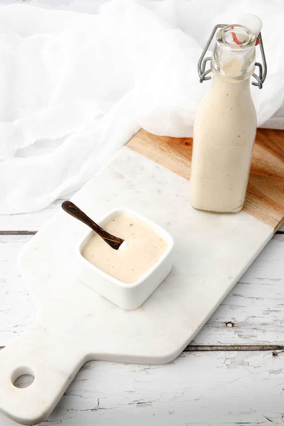 Homemade Caesar dressing in a bottle on a white board background