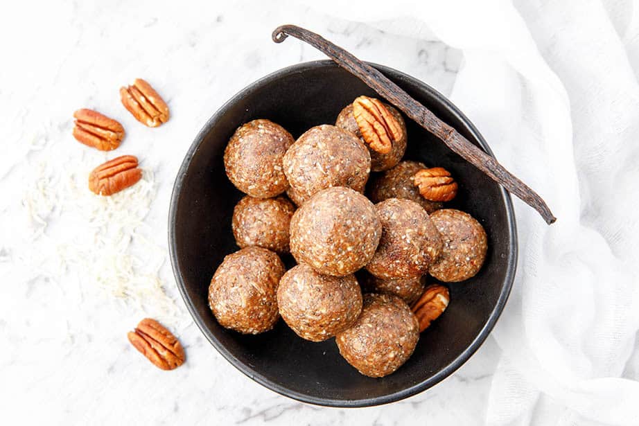 Overhead Salted Pecan Pie Bliss Balls in a bowl with vanilla bean and pecan nuts on a white background