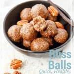 Captioned image of a bowl of Salted Pecan Pie Bliss Balls on a white background. One bite taken from the bliss ball.