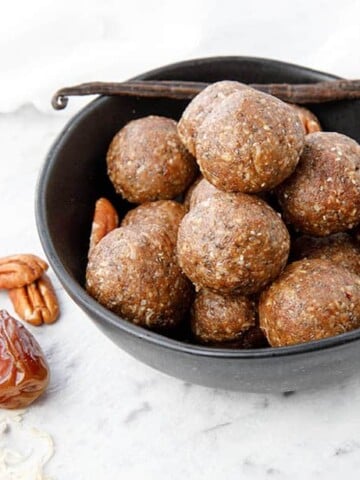 Thermomix Salted Pecan Bliss Balls on a white background, pecans and vanilla bean in photo