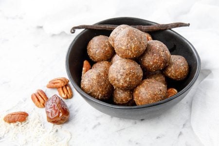 Thermomix Salted Pecan Bliss Balls on a white background, pecans and vanilla bean in photo