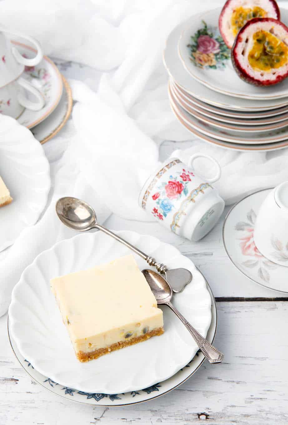 Passionfruit slice on a white wood background surrounded in a collection of crockery.