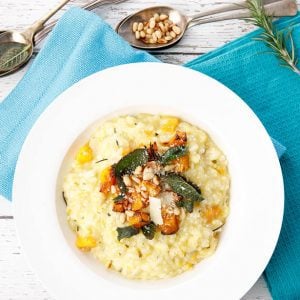 Overhead shot of pumpkin risotto in white bowl with blue napkin