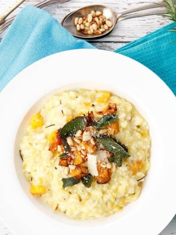 Overhead shot of pumpkin risotto in white bowl with blue napkin