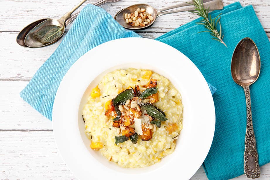 Overhead shot of pumpkin risotto in white bowl with blue napkin