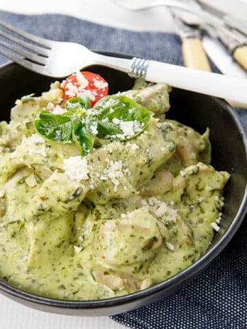 Landscape shot of creamy pesto chicken in a bowl on denim teatowel