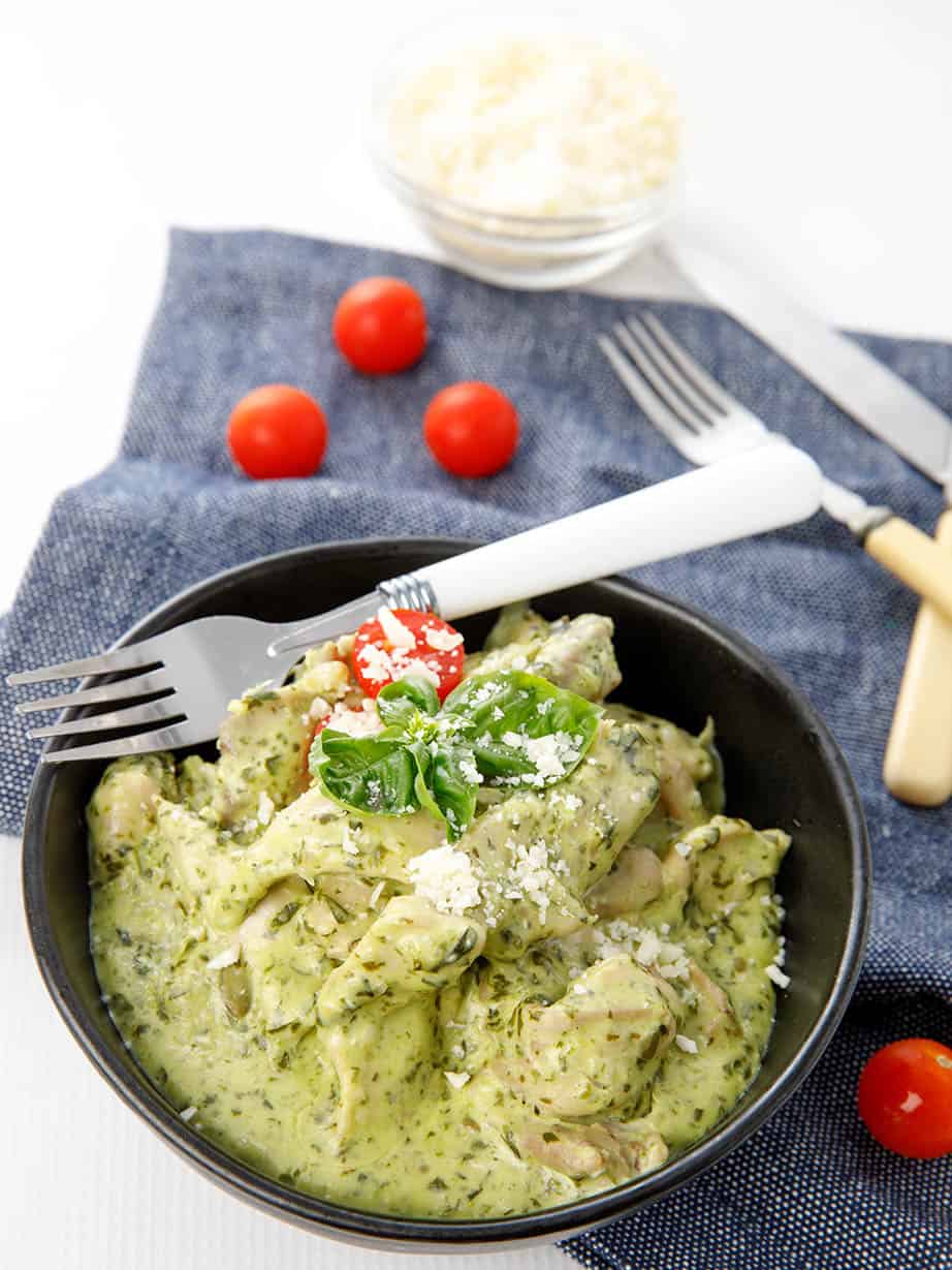 Potrait shot black bowl with chicken in a creamy pesto sauce