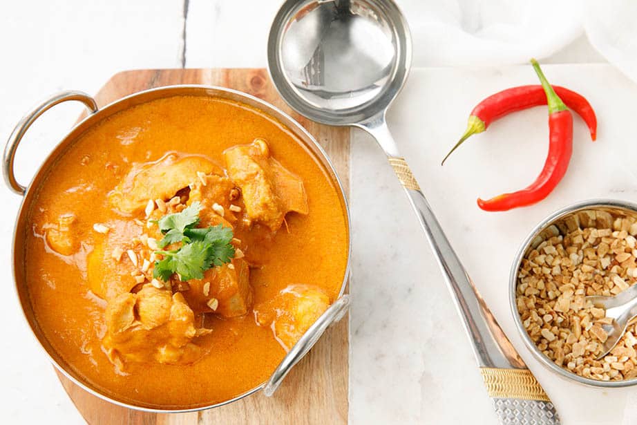 Overhead shot of Ghanaian Peanut Curry in a metal bowl on a white background