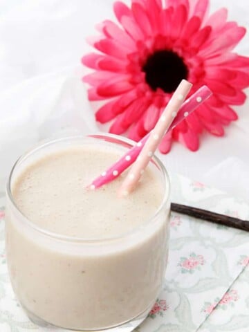Square image smoothie on napkin with a pink gerbra flower and vanilla bean