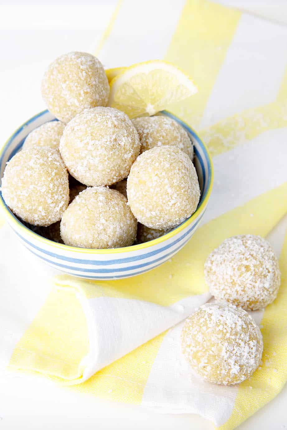 Portrait image of lemon bliss balls in a blue striped bowl on a yellow tea towel