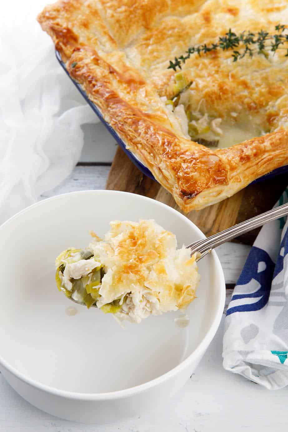 Chicken pie on a chopping board with a slice in a white bowl