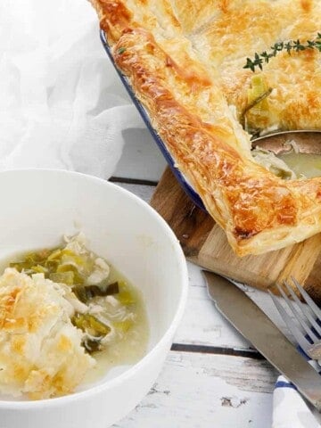 Square image chicken and leek pie on a white wood background