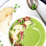 Overhead shot of green pea and ham soup in a white bowl topped with ham and parmesan cheese