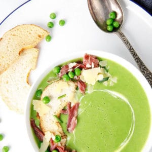 Overhead shot of green pea and ham soup in a white bowl topped with ham and parmesan cheese