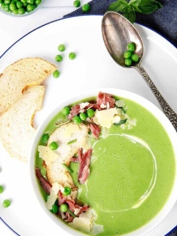 Overhead shot of green pea and ham soup in a white bowl topped with ham and parmesan cheese