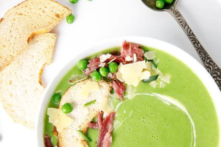 Overhead shot of green pea and ham soup in a white bowl topped with ham and parmesan cheese