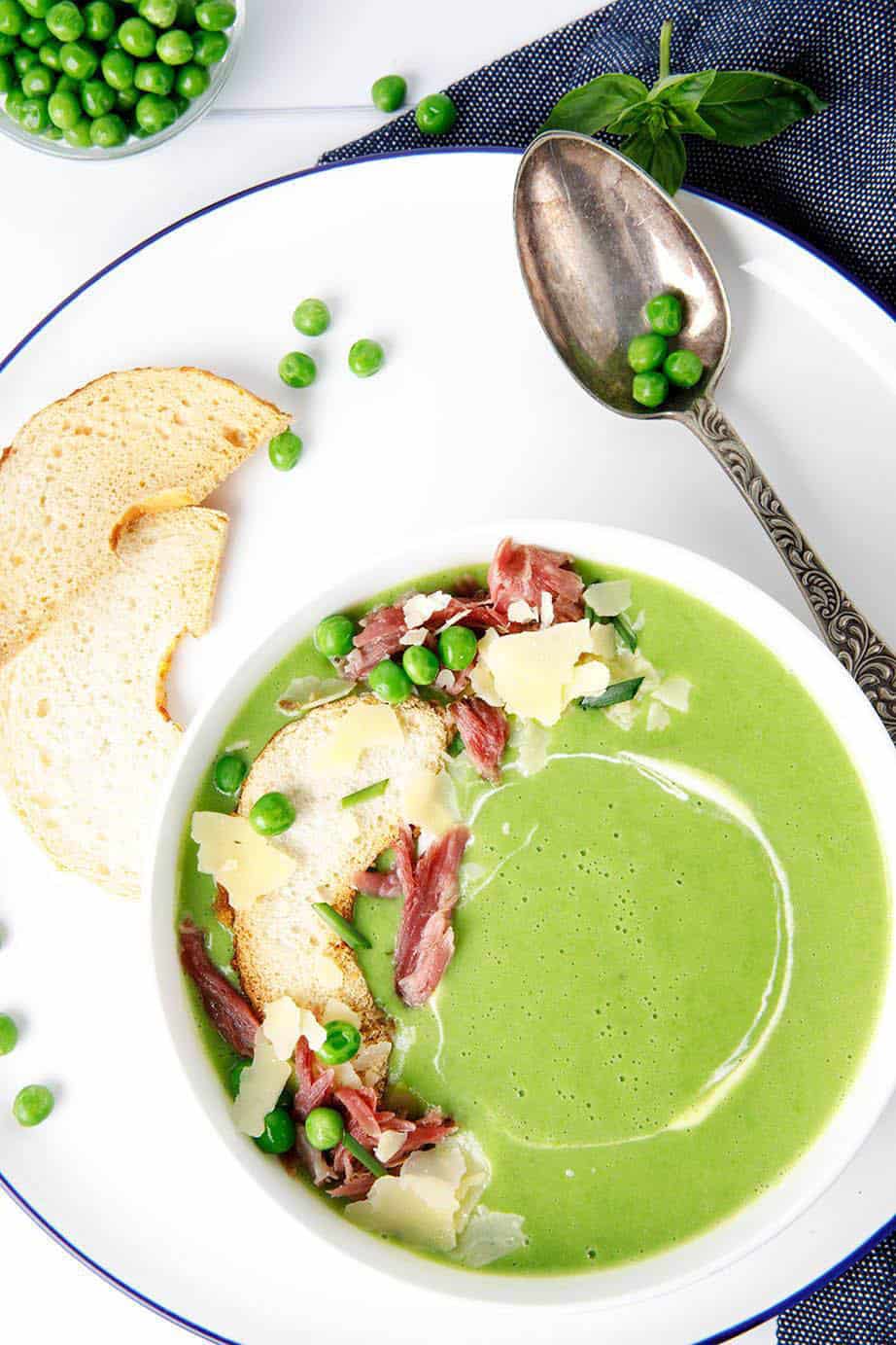Overhead shot of green pea ham soup in a white bowl topped with ham and parmesan cheese