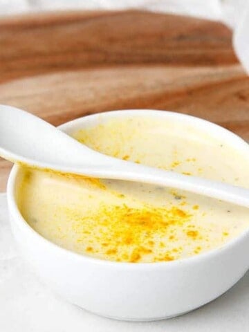 Close up of turmeric aioli in a white bowl on a chopping board