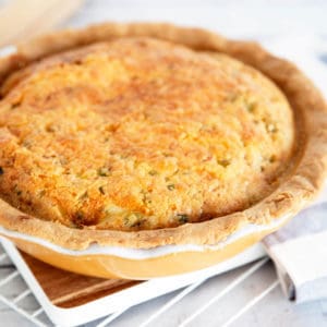 Portrait image of baked quiche Lorraine in a yellow pie dish on white cooling rack