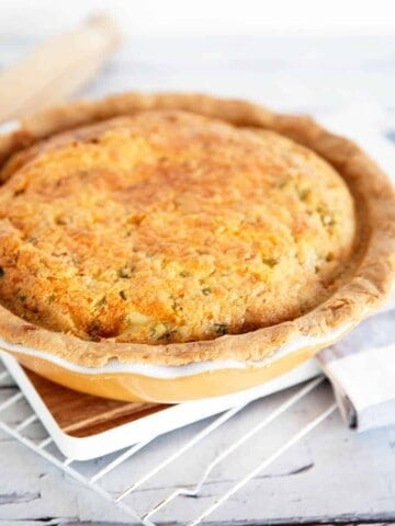 Portrait image of baked quiche Lorraine in a yellow pie dish on white cooling rack