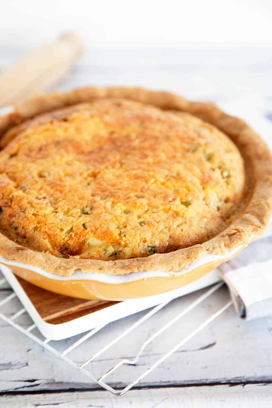 Portrait image of baked quiche Lorraine in a yellow pie dish on white cooling rack