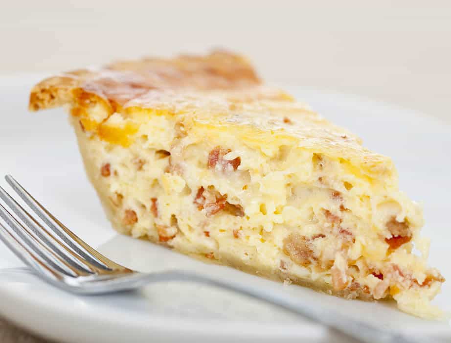 A single lice of quiche Lorraine on a white plate with fork