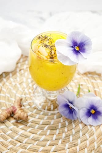 Turmeric Mango Smoothie on white background decorated with purple flowers and chia seeds
