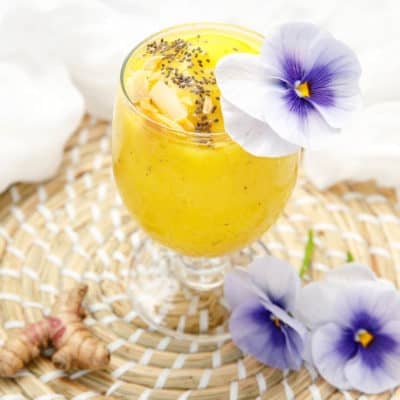 Turmeric Mango Smoothie on white background decorated with purple flowers and chia seeds