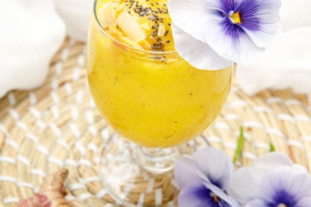 Turmeric Mango Smoothie on white background decorated with purple flowers and chia seeds