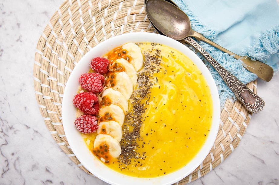 Turmeric Mango Smoothie Bowl decorated with banana, raspberry and black chia seeds