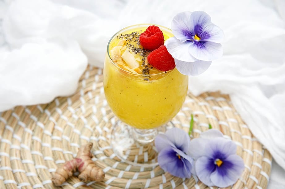 Glass containing turmeric mango smoothie decorated with raspberry and chia seeds