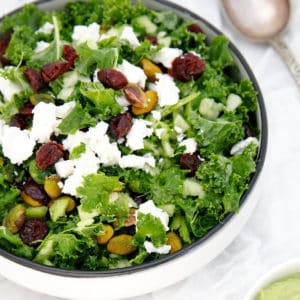 Potrait image of kale salad on a white cloth with cranberries and nuts
