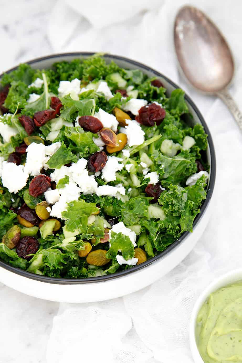 Potrait image of kale salad on a white cloth with cranberries and nuts