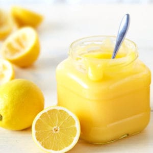 Lemon curd in glass jar with spoon on light wood background