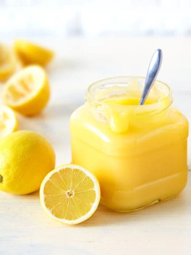 Lemon curd in glass jar with spoon on light wood background