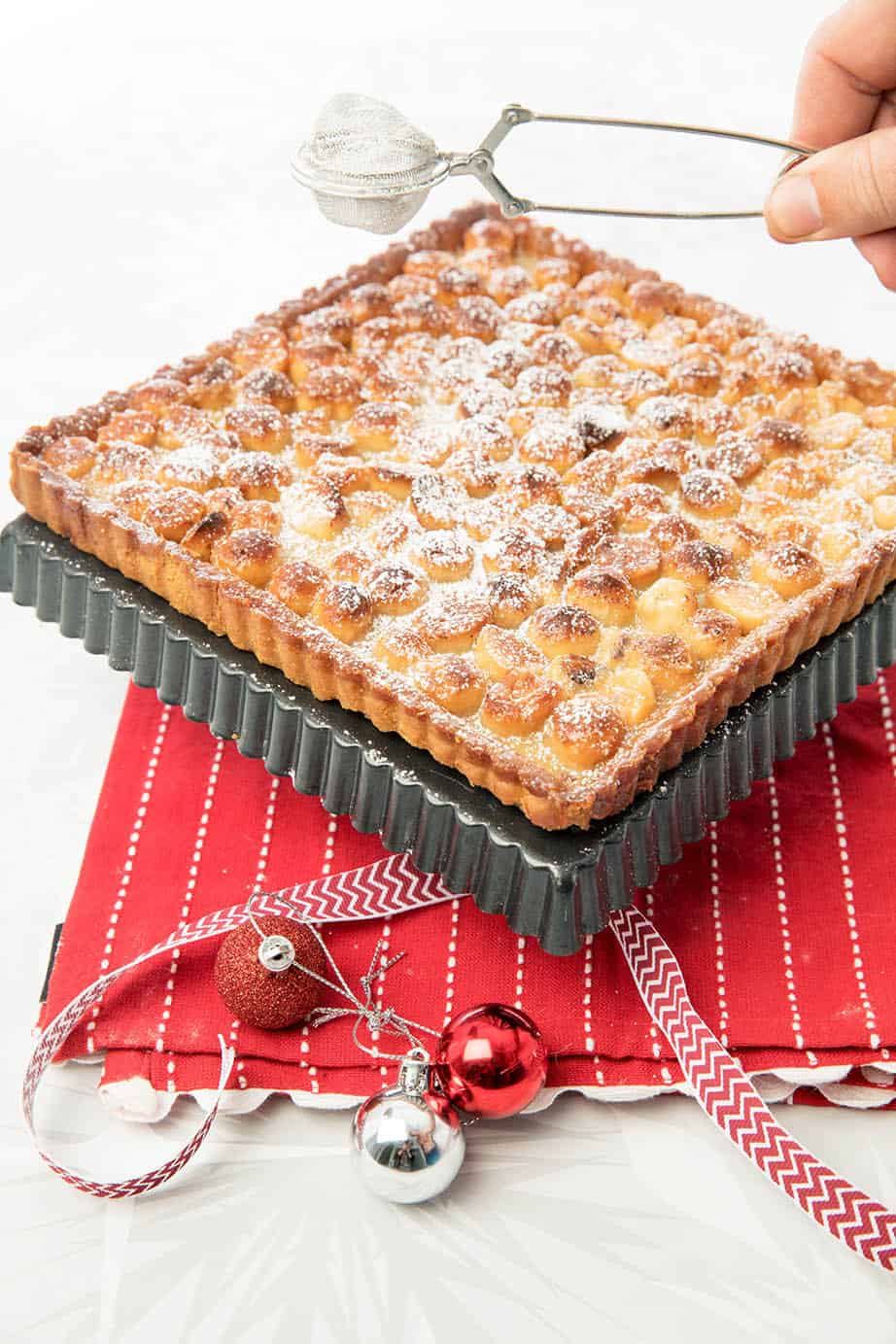 Macadamia Tart on red tea towel being dusted with icing sugar 