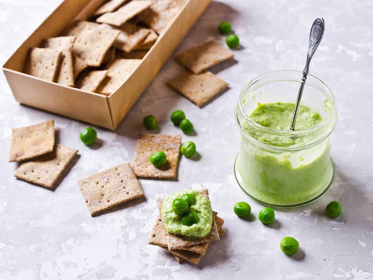 Overhead close up of smashed Bean with feta  and Pea Dip and crackers on a grey background and a cracker box