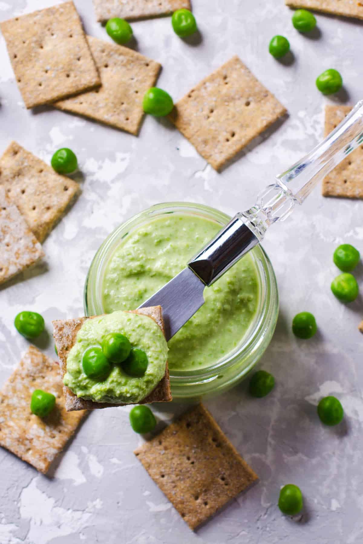Overhead close up of smashed Bean and Pea Dip and crackers on a grey background