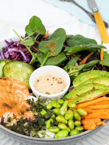 Poke bowl on a grey plate and white background include salad items and salmon