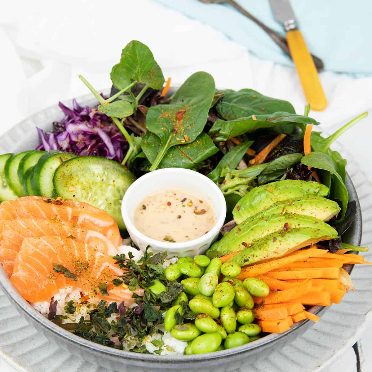 Poke bowl on a grey plate and white background include salad items and salmon