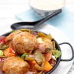 Sweet and sour pork meatballs on a black bowl white background with rice