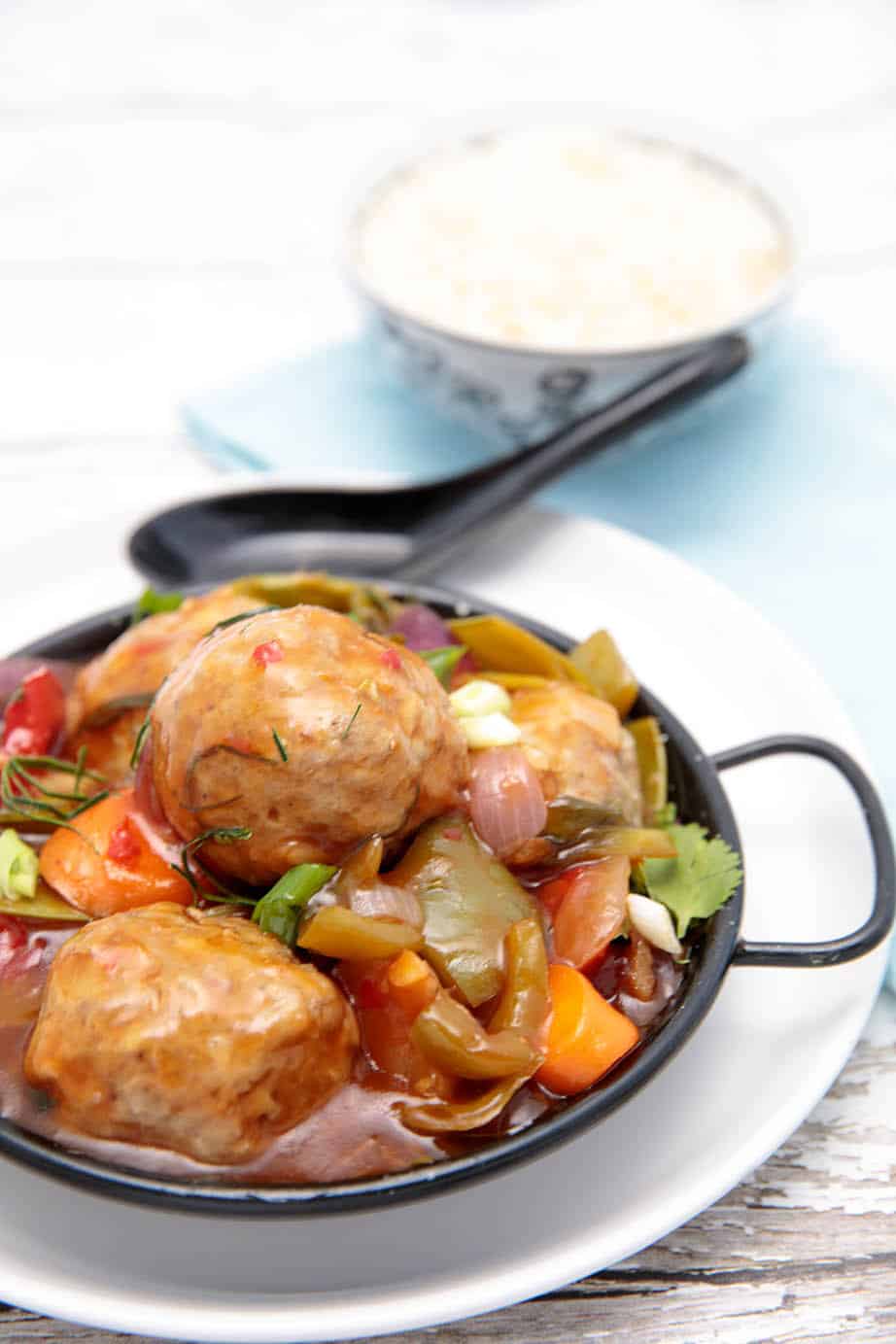 Sweet and sour pork meatballs on a black bowl white background with rice